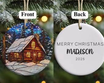 May include: A circular Christmas decoration featuring a winter cabin illustration on the front and the text "MERRY CHRISTMAS MADISON 2025" on the reverse. The cabin is brown with a snowy roof, set against a blue and white winter night scene.