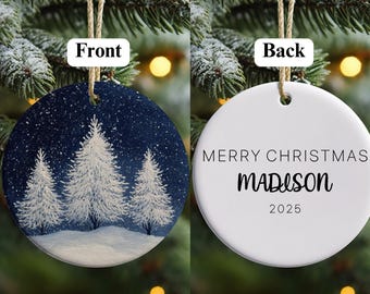 May include: A circular Christmas bauble with a winter scene on the front and text on the back. The front shows white pine trees against a dark blue snowy sky. The back says "MERRY CHRISTMAS MADISON 2025".