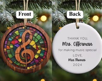 Pode incluir: Um enfeite de Natal de madeira com um design de clave de sol de vitral colorido na frente. A parte de trás do enfeite tem uma mensagem personalizada que diz "OBRIGADA, Sra. Offerman por tornar a música especial AMOR, Mia Thomas 2024".