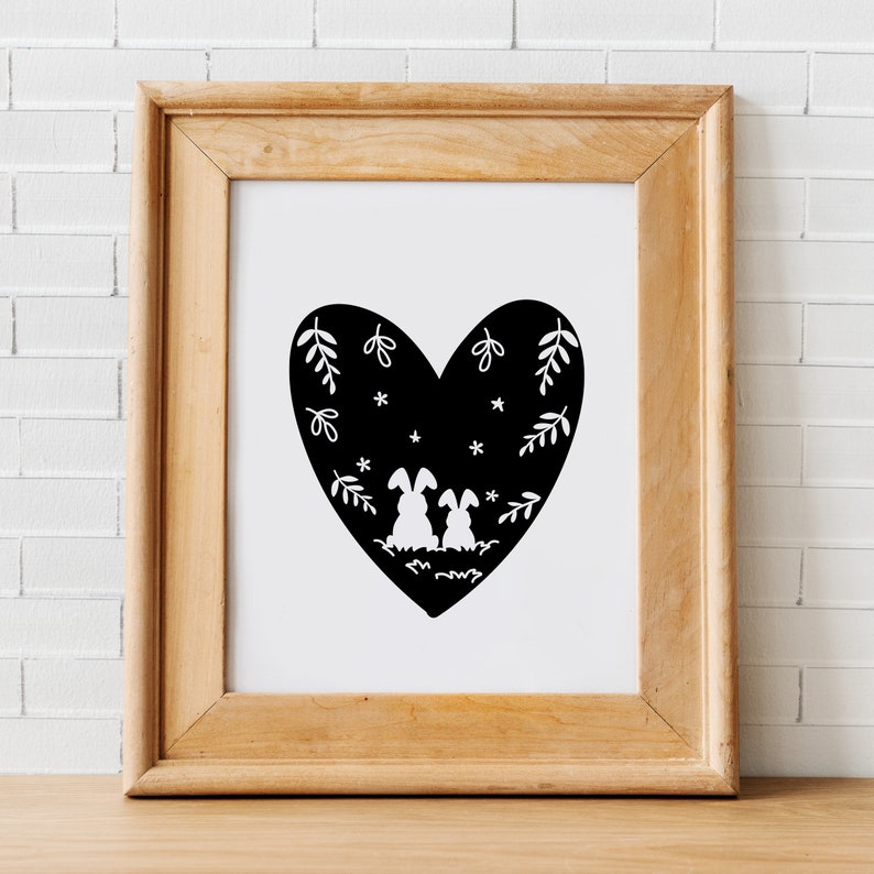 May include: A black and white illustration of two bunnies sitting inside a heart-shaped silhouette. The heart is filled with small white stars and stylized leaves.