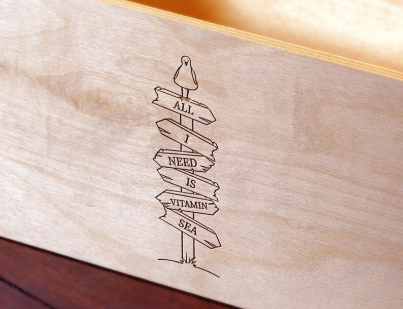 Puede incluir: Letrero de madera con el texto "ALL I NEED IS VITAMIN SEA" grabado en la madera. Un peque&ntilde;o p&aacute;jaro est&aacute; posado en la parte superior del poste indicador. El letrero es de madera clara.