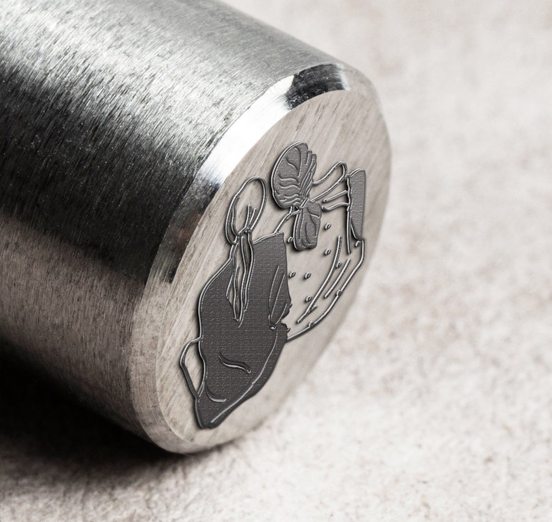 K&ouml;nnte beinhalten: Ein Stempel aus silbernem Metall mit einem Design aus zwei Figuren, die sich die H&auml;nde halten. Die Figuren sind stilisiert und haben ein schlichtes, minimalistisches Design.