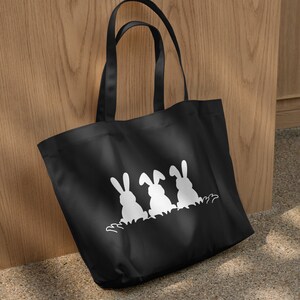 May include: Black tote bag with three white bunny silhouettes in a row. The bunnies are facing away from the viewer and have their ears up.