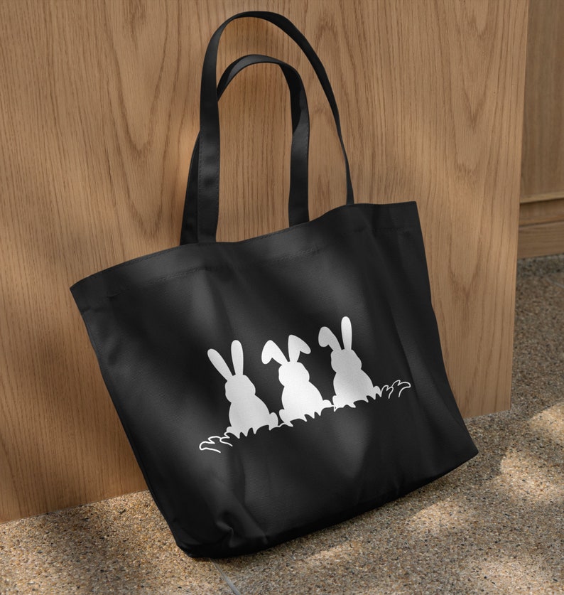 May include: Black tote bag with three white bunny silhouettes in a row. The bunnies are facing away from the viewer and have their ears up.