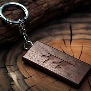 May include: A dark brown wooden keychain with a silver key ring and a carved design of two stylized butterflies. The keychain is lying on a wooden surface.