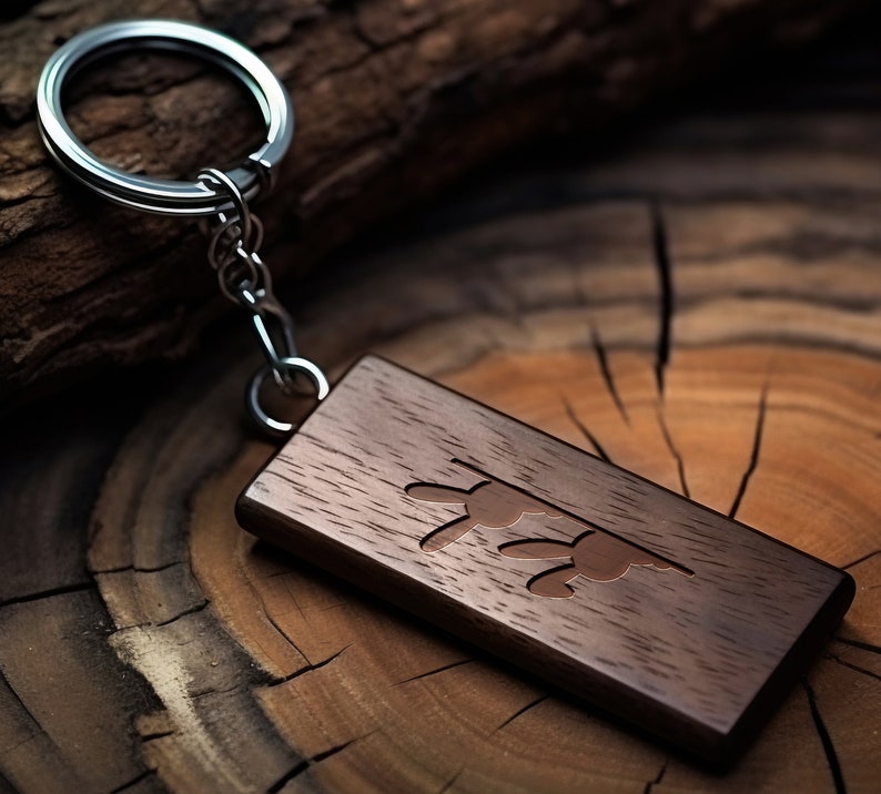 May include: A dark brown wooden keychain with a silver key ring and a carved design of two stylized butterflies. The keychain is lying on a wooden surface.
