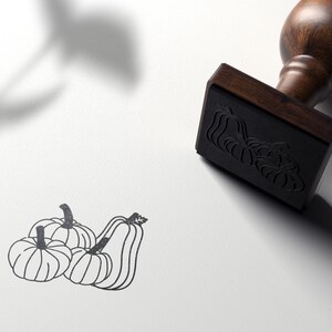 Puede incluir: Un dibujo en blanco y negro de cuatro calabazas. El dibujo est&aacute; en un sello de madera con un mango marr&oacute;n.