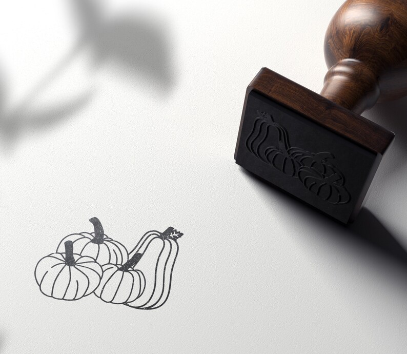 Puede incluir: Un dibujo en blanco y negro de cuatro calabazas. El dibujo est&aacute; en un sello de madera con un mango marr&oacute;n.
