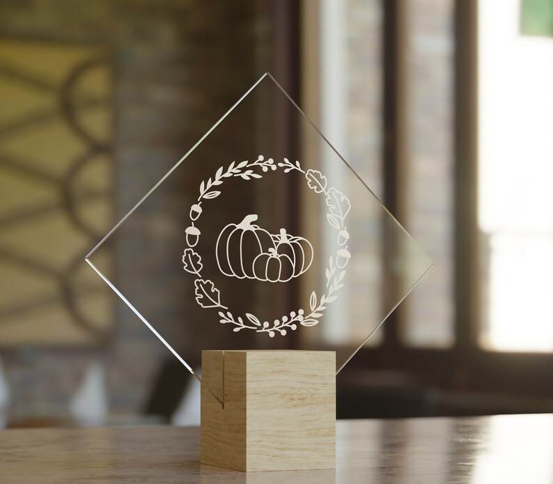 Puede incluir: Una placa de vidrio transparente en forma de diamante con un dise&ntilde;o grabado en blanco de calabazas y follaje de oto&ntilde;o. La placa est&aacute; sobre una base de madera.
