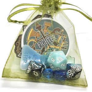 May include: A green mesh bag filled with various dice and a round card with the word "Fighter" on it.