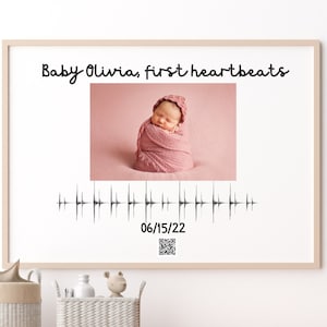 Könnte beinhalten: Ein gerahmter Druck mit einem Foto eines Babys, das in einem rosa Swaddle schläft. Der Druck enthält auch den Text "Baby Olivia, first heartbeats" und ein Sonogramm-Bild mit dem Datum "06/15/22".