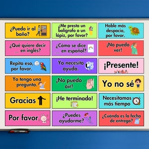 May include: A white board with colourful squares containing Spanish phrases and illustrations. The phrases include "Puedo ir al ba&ntilde;o?" (Can I go to the bathroom?), "&iquest;Qu&eacute; quiere decir en ingl&eacute;s?" (What does it mean in English?), "Repita eso, por favor." (Repeat that, please), "Yo tengo una pregunta." (I have a question), "Gracias" (Thank you), "Por favor" (Please), "&iquest;Me presta un bol&iacute;grafo o un l&aacute;piz, por favor?" (Can I borrow a pen or pencil, please?), "&iquest;C&oacute;mo se dice en espa&ntilde;ol?" (How do you say it in Spanish?), "Yo necesito ayuda." (I need help), "Hable m&aacute;s despacio, por favor." (Speak slower, please), "&iexcl;No puedo ver!" (I can't see!), "&iexcl;Presente!" (Present!), "&iexcl;No puedo o&iacute;r!" (I can't hear!), "Yo no s&eacute;" (I don't know), "&iexcl;He terminado!" (I'm finished!), "Necesitamos m&aacute;s tiempo." (We need more time), "&iquest;Puedes ayudarme?" (Can you help me?), and "&iquest;Cu&aacute;ndo es la fecha de entrega?" (When is the due date?).