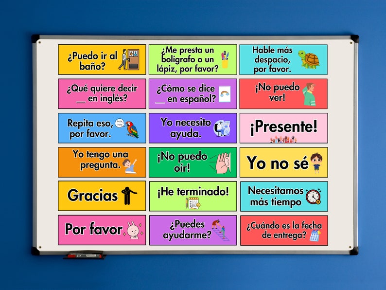 May include: A white board with colourful squares containing Spanish phrases and illustrations. The phrases include "Puedo ir al ba&ntilde;o?" (Can I go to the bathroom?), "&iquest;Qu&eacute; quiere decir en ingl&eacute;s?" (What does it mean in English?), "Repita eso, por favor." (Repeat that, please), "Yo tengo una pregunta." (I have a question), "Gracias" (Thank you), "Por favor" (Please), "&iquest;Me presta un bol&iacute;grafo o un l&aacute;piz, por favor?" (Can I borrow a pen or pencil, please?), "&iquest;C&oacute;mo se dice en espa&ntilde;ol?" (How do you say it in Spanish?), "Yo necesito ayuda." (I need help), "Hable m&aacute;s despacio, por favor." (Speak slower, please), "&iexcl;No puedo ver!" (I can't see!), "&iexcl;Presente!" (Present!), "&iexcl;No puedo o&iacute;r!" (I can't hear!), "Yo no s&eacute;" (I don't know), "&iexcl;He terminado!" (I'm finished!), "Necesitamos m&aacute;s tiempo." (We need more time), "&iquest;Puedes ayudarme?" (Can you help me?), and "&iquest;Cu&aacute;ndo es la fecha de entrega?" (When is the due date?).