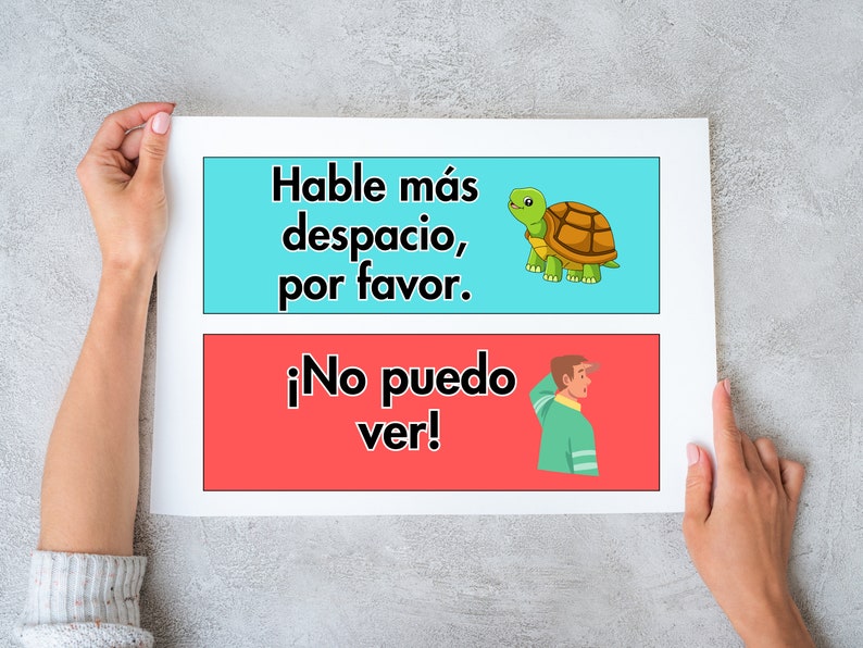 May include: Two colourful signs with Spanish text. The top sign is blue and says "Hable m&aacute;s despacio, por favor." with a cartoon tortoise. The bottom sign is red and says "&iexcl;No puedo ver!" with a cartoon person looking over their shoulder.