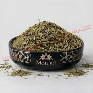 Può includere: Una ciotola in ceramica nera riempita con un mucchio di steli di erbe essiccate verdi. La ciotola presenta un'icona di fiore di loto dorato e il testo MonJad stampato sul davanti, insieme a un motivo geometrico ripetuto sul bordo.
