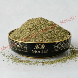 May include: A black ceramic bowl filled with a mound of dried green herbs. The bowl features a gold lotus flower graphic and the text MonJad printed in gold. The exterior of the bowl is decorated with a repeating gold geometric floral pattern.