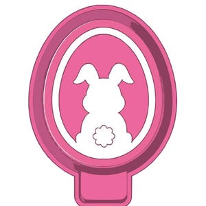Könnte beinhalten: Rosaer Oster-Eier-Ausstecher mit einer weißen Hasensilhouette im Inneren. Der Hase hat eine Blume am Schwanz.