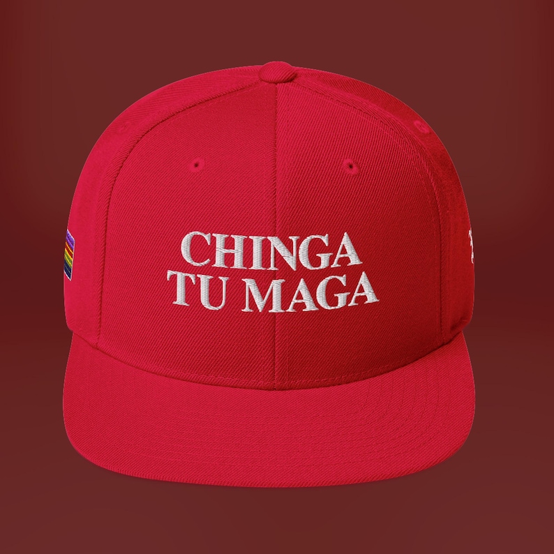 K&ouml;nnte beinhalten: Rote Baseballkappe mit einem wei&szlig;en gestickten Spruch "CHINGA TU MAGA" und einem Regenbogenstreifen an der Seite.