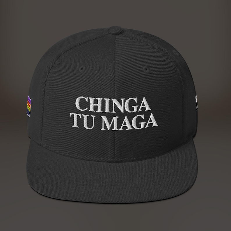 K&ouml;nnte beinhalten: Schwarze Baseballkappe mit einem wei&szlig;en gestickten Spruch "CHINGA TU MAGA" und einer kleinen Regenbogenflagge an der Seite.