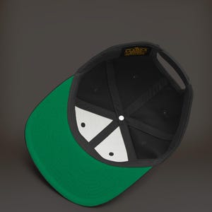 K&ouml;nnte beinhalten: Schwarze und gr&uuml;ne Baseballkappe mit wei&szlig;em Innenfutter. Die Kappe hat ein Etikett mit der Aufschrift "The Classics" in goldenen Buchstaben.