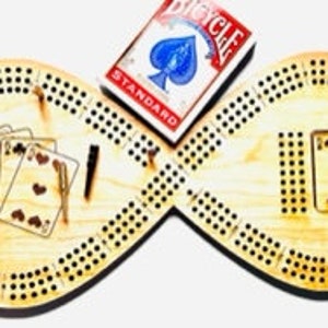 Puede incluir: Un tablero de cribbage de madera con forma de símbolo de infinito. El tablero tiene dos superficies de juego con agujeros para clavijas y un espacio para una baraja de cartas. El tablero está hecho de madera clara y tiene un acabado natural.