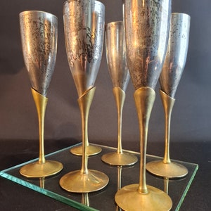 Può includere: Sei flute da champagne argentate con steli e basi dorate, disposte su un vassoio di vetro trasparente.