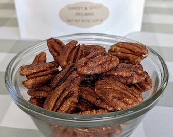 May include: A glass bowl filled with sweet and spicy pecans. The pecans are a deep brown color and have a glossy finish.