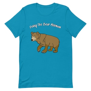 Puede incluir: Una camiseta azul turquesa con un oso marrón de dibujos animados y el texto "Doing The Bear Minimum".