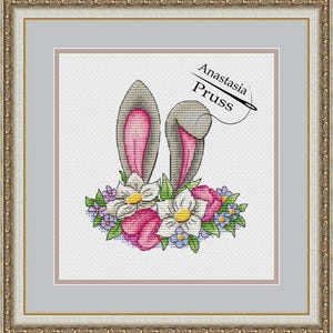 May include: Cross stitch pattern featuring a bunny's ears with pink and gray details, surrounded by a wreath of flowers in shades of pink, white, and purple. The pattern is titled "Anastasia Pruss".