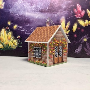 Op de afbeelding: Een miniatuurhuisornament met een bruin dak en beige muren. Het huis is versierd met kleurrijke bloemen en heeft een kleine deur en een raam. De achtergrond bevat illustraties van kristallen en een donkerpaarse lucht.