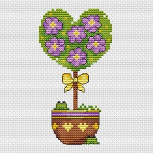 Peut inclure: Motif de point de croix d'un topiaire en forme de cœur avec des fleurs violettes et un nœud jaune. Le topiaire est dans un pot marron avec une bande violette et des cœurs jaunes. Deux grenouilles vertes sont visibles.