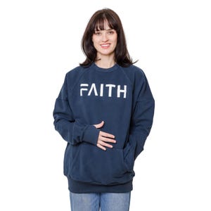 May include: A navy blue sweatshirt with a large white graphic that says "FAITH" on the front. The sweatshirt has a kangaroo pocket and a ribbed hem.