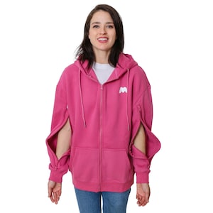 May include: A pink zip-up hoodie with a white logo on the front. The sleeves have a unique design with openings at the elbows.