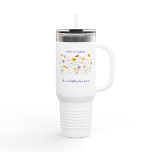 May include: White travel mug with a handle and a straw. The mug features a floral design with the text "meet me where the wildflowers grow" in blue and yellow. The mug is designed to keep beverages hot or cold.