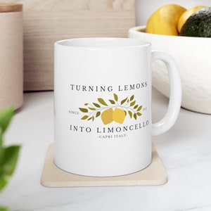 May include: White ceramic mug with a black graphic that says "Turning Lemons into Limoncello - Capri Italy - Since 1913". The graphic also features two yellow lemons on a green branch with leaves.