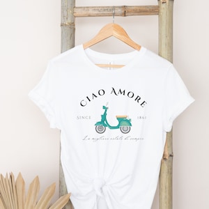 Op de afbeelding: Wit T-shirt met een groene vintage scooter afbeelding en de tekst "Ciao Amore Since 1861 La migliore estate di sempre".