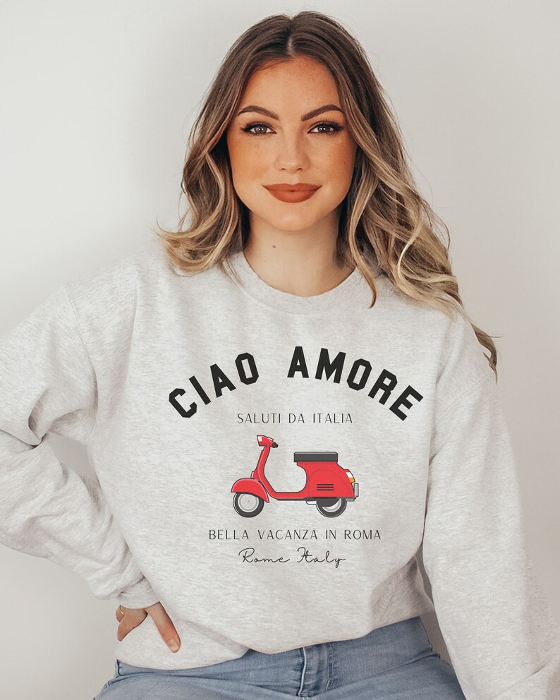 Op de afbeelding: Grijs sweatshirt met een zwarte grafische print van een rode scooter en de tekst "Ciao Amore", "Saluti da Italia", "Bella Vacanza in Roma" en "Rome Italy".