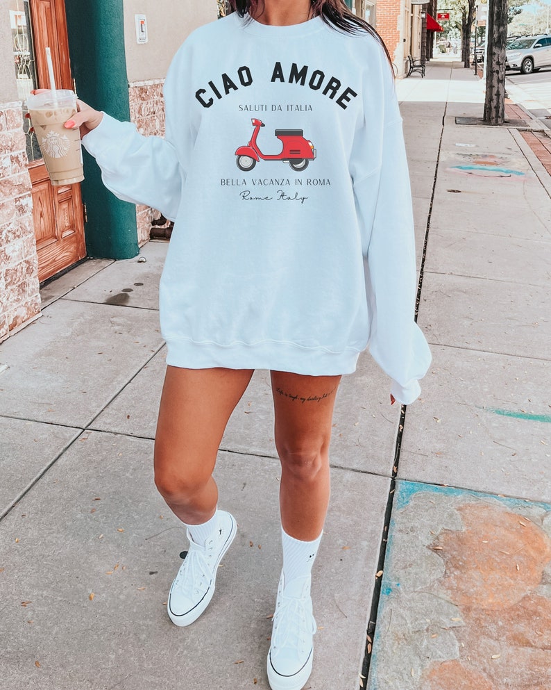 Op de afbeelding: Wit sweatshirt met een rode scooter afbeelding en de tekst "Ciao Amore Saluti da Italia Bella Vacanza in Roma Rome Italy".