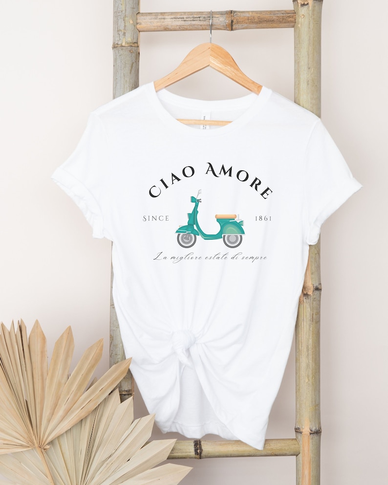 Op de afbeelding: Wit T-shirt met een groene vintage scooter afbeelding en de tekst "Ciao Amore Since 1861 La migliore estate di sempre".