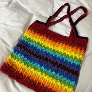 May include: A rainbow crochet tote bag with black straps. The bag is made with a variety of colors, including red, orange, yellow, green, blue, indigo, and violet.