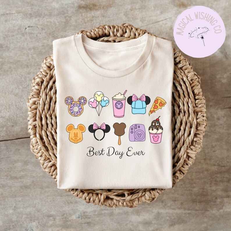 Może przedstawiać: Jasnoszary t-shirt z grafiką przedstawiającą r&oacute;żne ikony związane z Disneyem, w tym uszy Myszki Miki, pączek, balony, nap&oacute;j, czapkę, kawałek pizzy, loda na patyku, aparat fotograficzny i lody. Pod ikonami znajduje się napis "Best Day Ever".