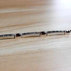 May include: A silver bracelet with a row of small, dark red square stones and a row of smaller, dark green stones.