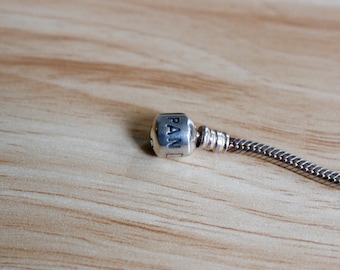 May include: A silver charm bracelet with a silver charm that says "PAN" on it.
