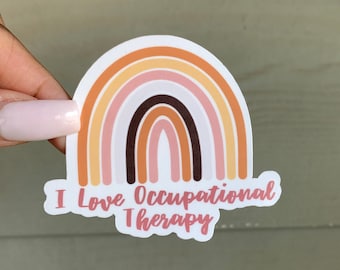Pode incluir: Um adesivo com um design de arco-íris em tons de laranja, rosa, marrom e branco. O texto "I Love Occupational Therapy" está escrito abaixo do arco-íris.