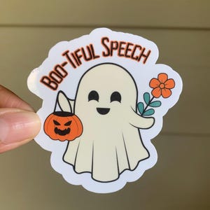 以下が含まれることがあります： 優しい顔をした白い幽霊が、カボチャのバケツと花を持っています。白い背景に黒い文字で「BOO-TIFUL SPEECH」と書かれています。