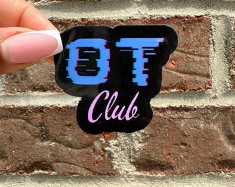 Puede incluir: Pegatina negra con el texto "OT Club" en azul y rosa. Las letras "OT" tienen un efecto de fallo. La pegatina se sostiene contra una pared de ladrillos.