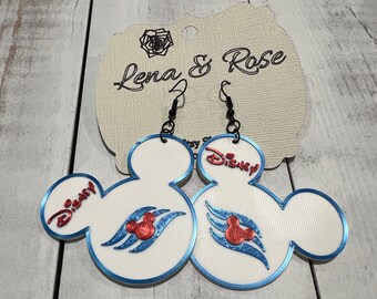 Puede incluir: Un par de pendientes blancos con forma de Mickey Mouse con detalles en azul y rojo. Los pendientes tienen la palabra "Disney" y una cabeza de Mickey Mouse estilizada con tres olas. Los pendientes cuelgan de ganchos negros.