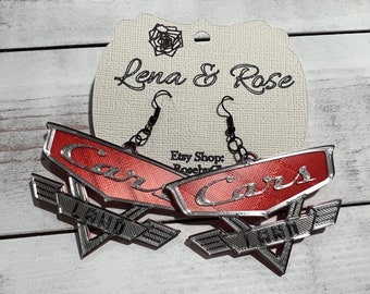 May include: Red and silver earrings with the words "Cars Land" on them. The earrings are shaped like the logo for the Cars movie.