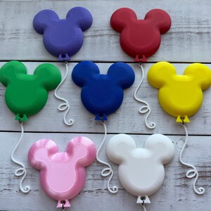 May include: A collection of seven 3D-printed balloon-shaped ornaments in the silhouette of a mouse head. The colors include purple, red, green, blue, yellow, pink, and white. Each ornament features a white, curly, attached string.
