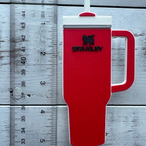 Close up of red Stanley tumbler charm shown next to a US ruler.  It is approximately 5 inches from tip of straw to bottom of cup.  It is about 2.25 inches wide at the handle.